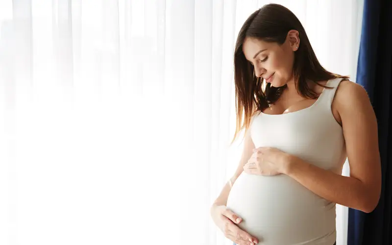 A pregnant woman smiling with her hands on her belly