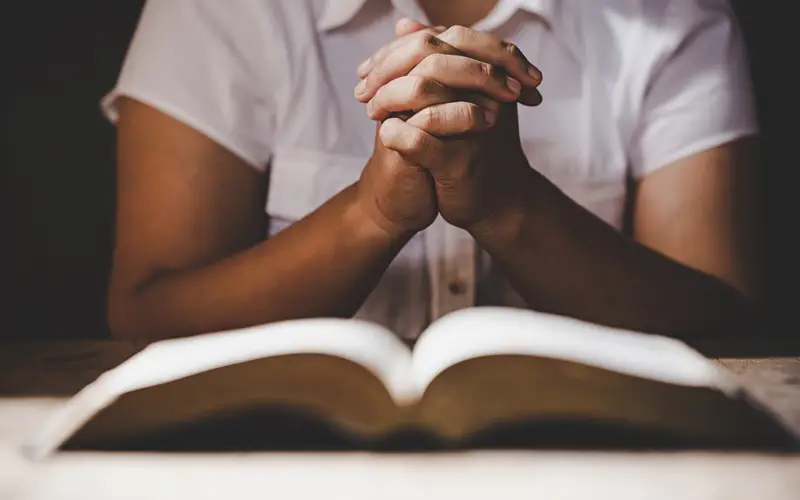 Hands folded in prayer over an open Bible