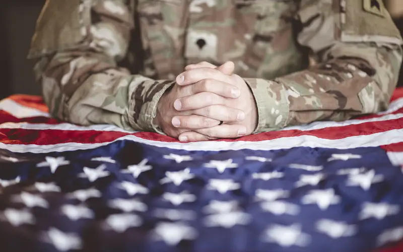 A service member in uniform with hands folded over an American flag
